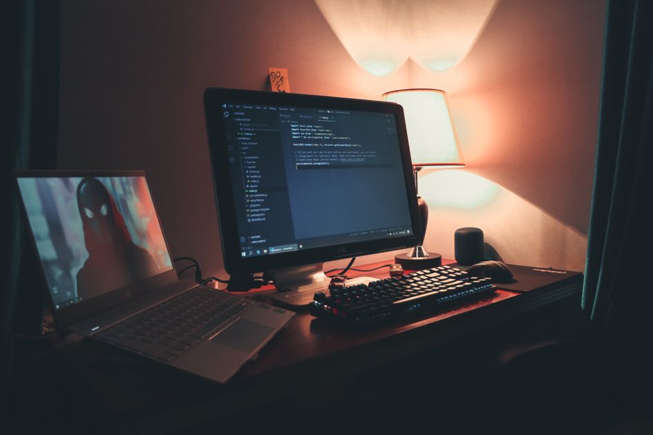 Home office dual-screen setup for remote game development work with warm lighting